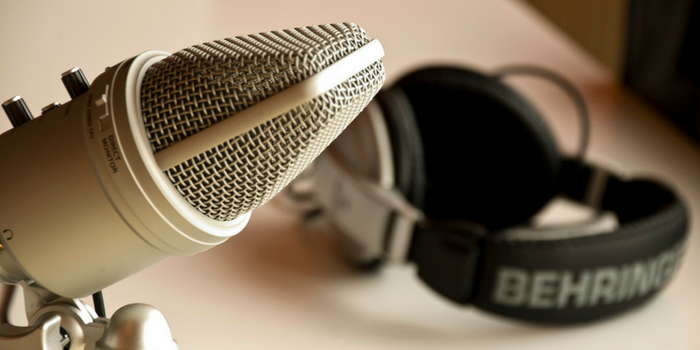 A close-up of a silver microphone in the foreground with a pair of black Behringer headphones resting in the blurred background.
