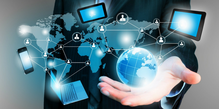 A person in a suit holds a glowing digital globe, with icons of laptops, tablets, and smartphones connected by lines overlaying a world map, symbolizing global digital connectivity and technology.