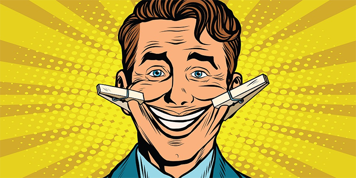 A cartoon man with blue eyes smiles widely while two clothespins pull the corners of his mouth up. The background features bright yellow rays and dots in a comic book style.