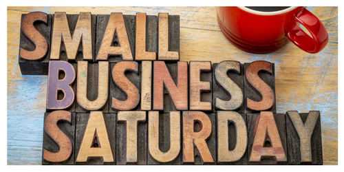 Wooden block letters spell Small Business Saturday on a colorful wooden table, with a red coffee cup in the top right corner.