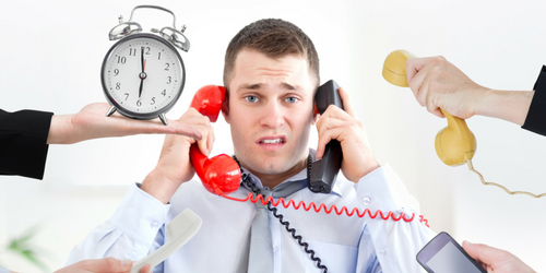 A stressed man in an office holds two phones to his ears while several hands offer more phones and a clock, symbolizing being overwhelmed and busy at work.