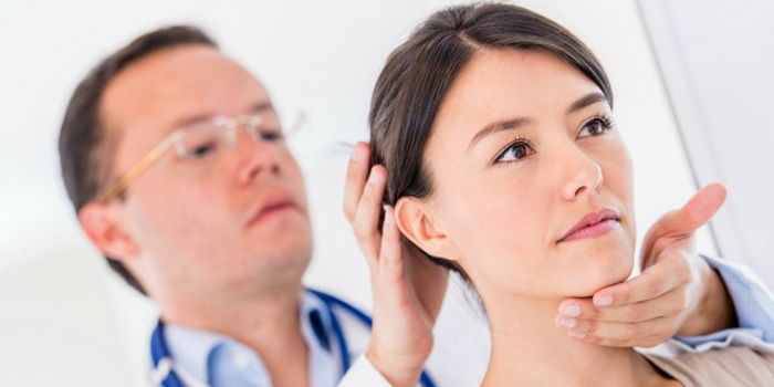 A doctor wearing glasses examines a womans neck and ear, gently holding her head with one hand and her chin with the other during a medical check-up.