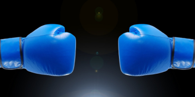 Abby-Connect-Vs-LexReception–Which-Is-Right-For-You Two blue boxing gloves face each other against a dark background, ready for a fight or competition—symbolizing the competitive edge that Abby Connect brings to your business.