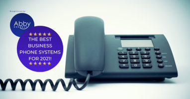 A black office phone with a cord is on a white surface. A purple circle on the left reads, The best business phone systems for 2021! with stars and the Abby Connect logo above it.