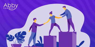 Illustration of three people on purple blocks helping each other climb upward, symbolizing teamwork and support. The background is purple with abstract shapes and a plant. Abby Connect logo appears in the top left corner.
