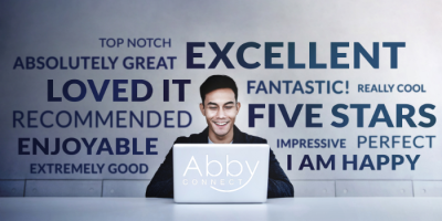 A smiling man sits at a desk using a laptop labeled Abby Connect, surrounded by positive words and phrases like EXCELLENT, FIVE STARS, LOVED IT, and RECOMMENDED on the wall behind him.