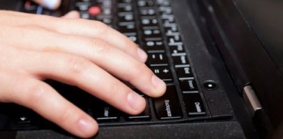 A close-up of a persons hand typing on a black laptop keyboard, with fingers resting on the Enter and Backspace keys.