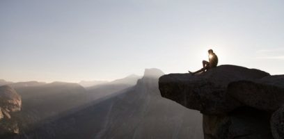 customer_service_blog_13 A person sits alone on the edge of a large rocky cliff overlooking a vast mountainous landscape at sunrise, contemplating how to test a new market as sunlight shines behind them.