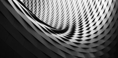 Curved architectural structure with a repeating geometric diamond pattern, creating a swirling, twisting effect in grayscale light and shadow.