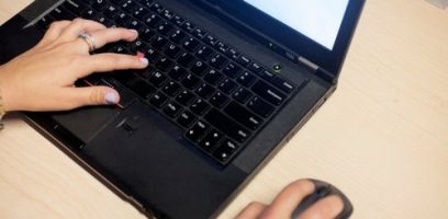 customer_service_blog_30 A person with painted nails types on a black laptop keyboard with one hand while using a wireless mouse with the other, on a light-colored desk.