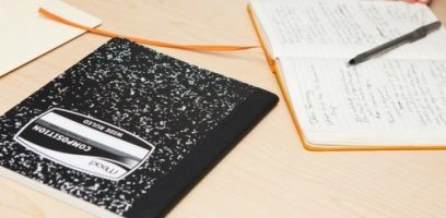 customer_service_blog_5 A black and white composition notebook and an open notebook with handwritten notes and a pen rest on a light wooden desk.