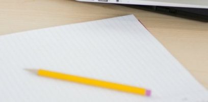 customer_service_blog_72 A yellow pencil rests on a lined sheet of paper with the corner of a laptop visible in the background on a light wooden desk.