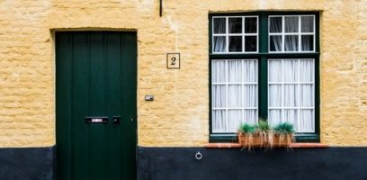 customer_service_blog_89 A yellow brick house with a dark green door, window frames, and a window box holding plants. The house number 2 is displayed between the door and window. The lower part of the wall is painted black.
