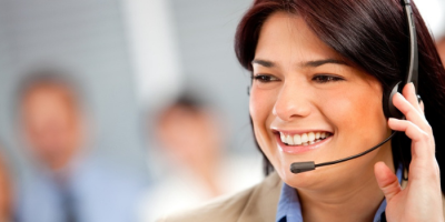 Smiling woman wearing a headset, possibly a customer service representative, with a blurred office background.