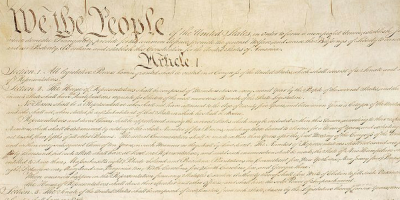 A close-up image of the handwritten United States Constitution, showing the iconic opening words We the People and the beginning text of Article I in ornate script on aged parchment.
